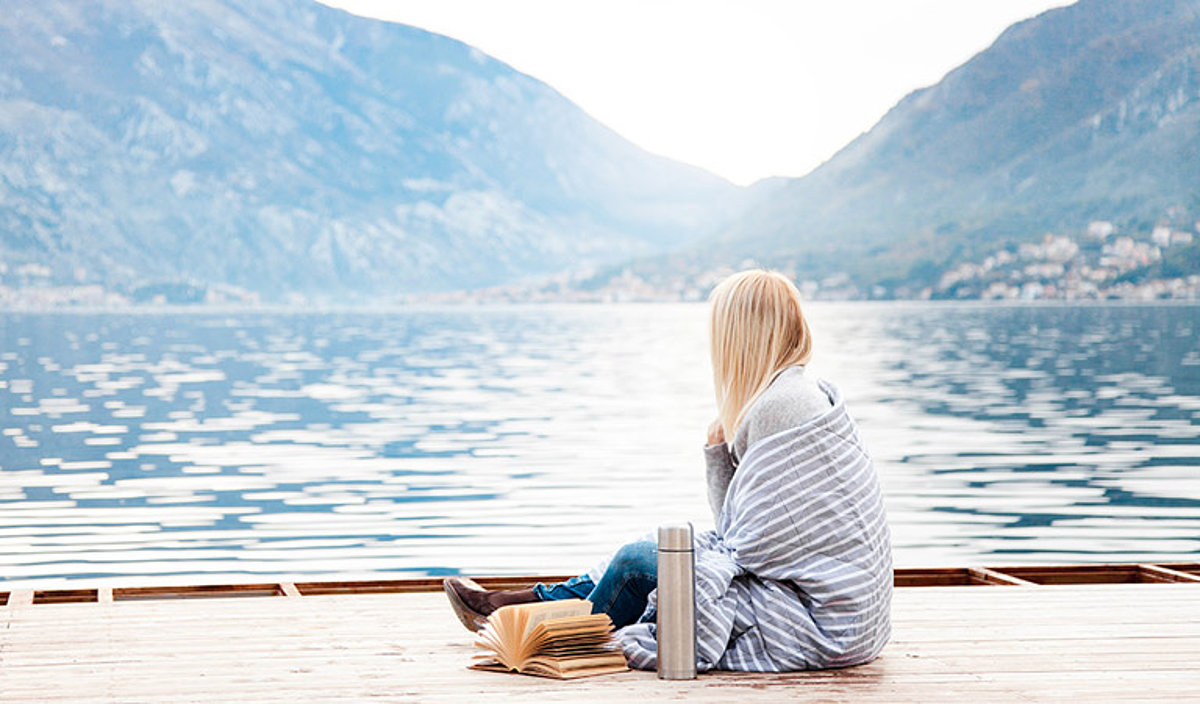 Junge Frau sitzt auf einem Bootssteeg mit abgewendetem Blick